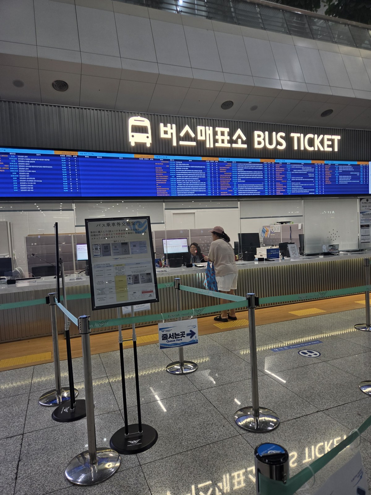 Staffed bus ticket counter beneath departure information boards at Terminal 2