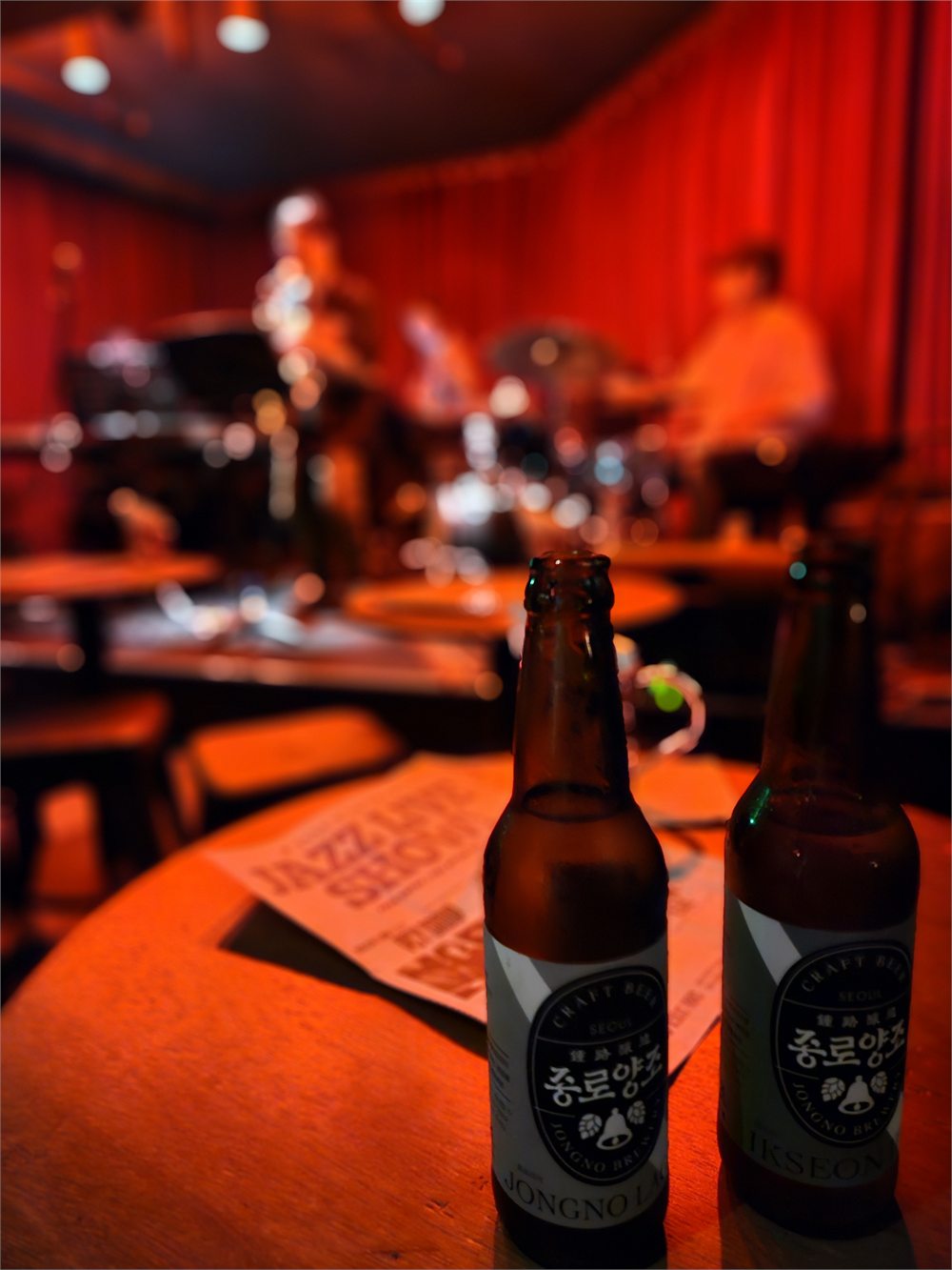 Two bottles of Jongno Brewery beer on a table in front of Subriot HBC's red-lit stage